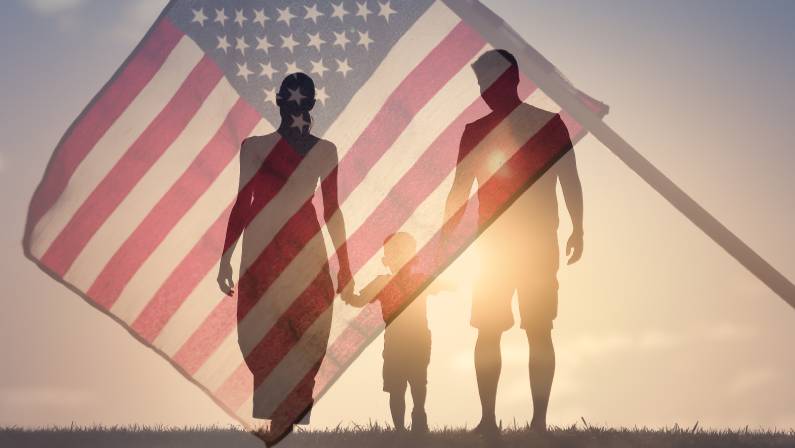 Happy family walking together at sunset holding hands agains the flag of America USA background